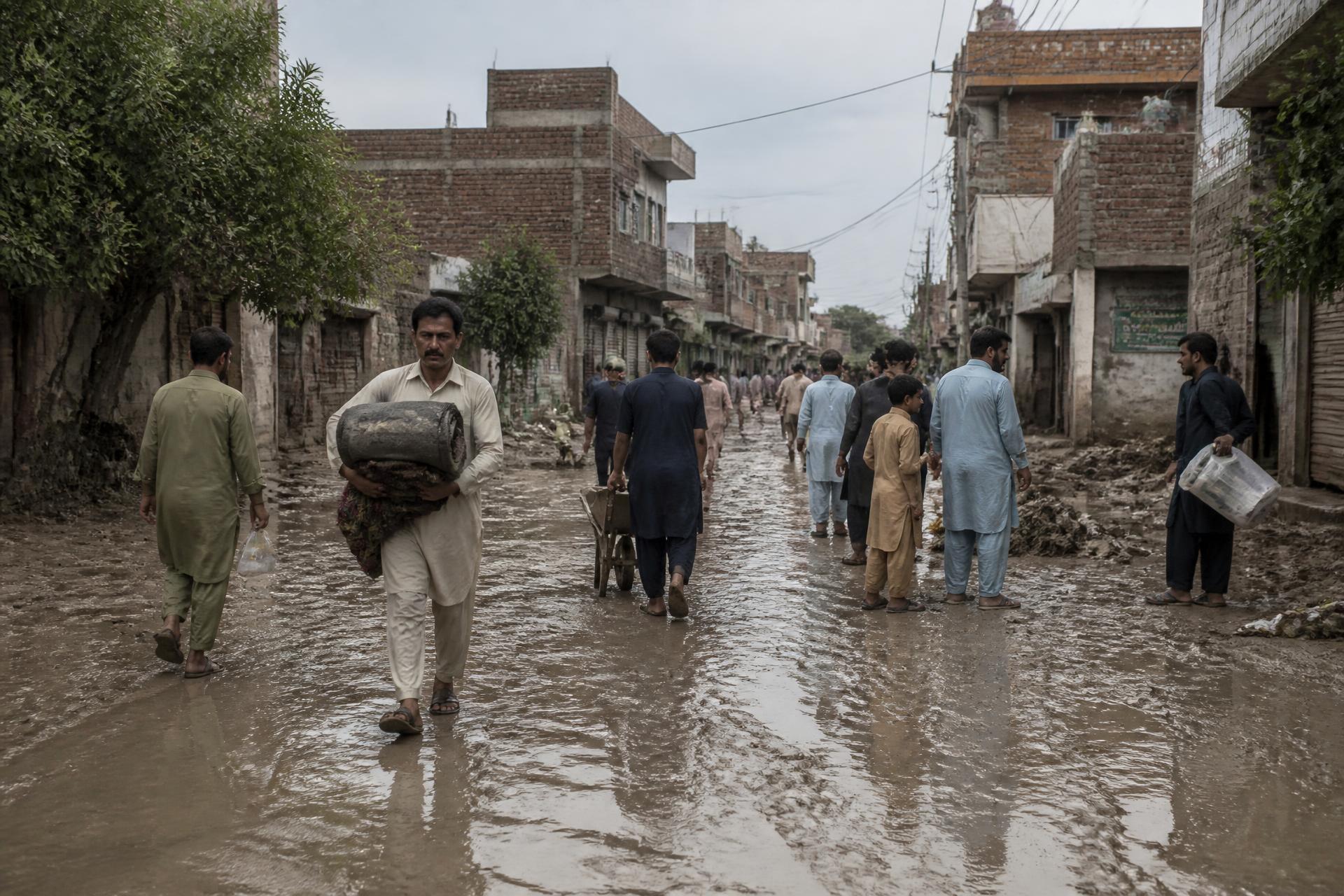 Residents of a Rawalpindi neighbourhood carrying belongings through a street after floodwater receded